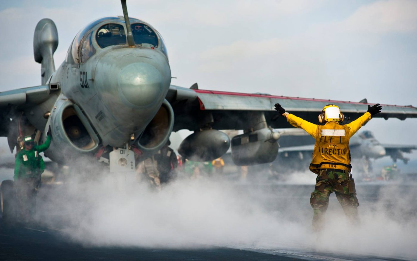 EA-6B Prowler on a carrier flight deck, directed by a yellow-shirt crew member
